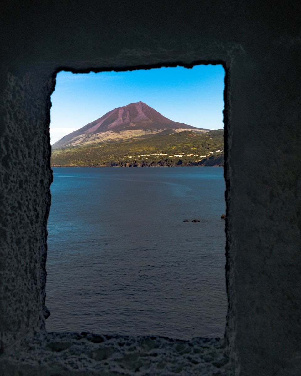 A montanha do Pico vista através da janela de uma construção em pedra, com o mar em primeiro plano